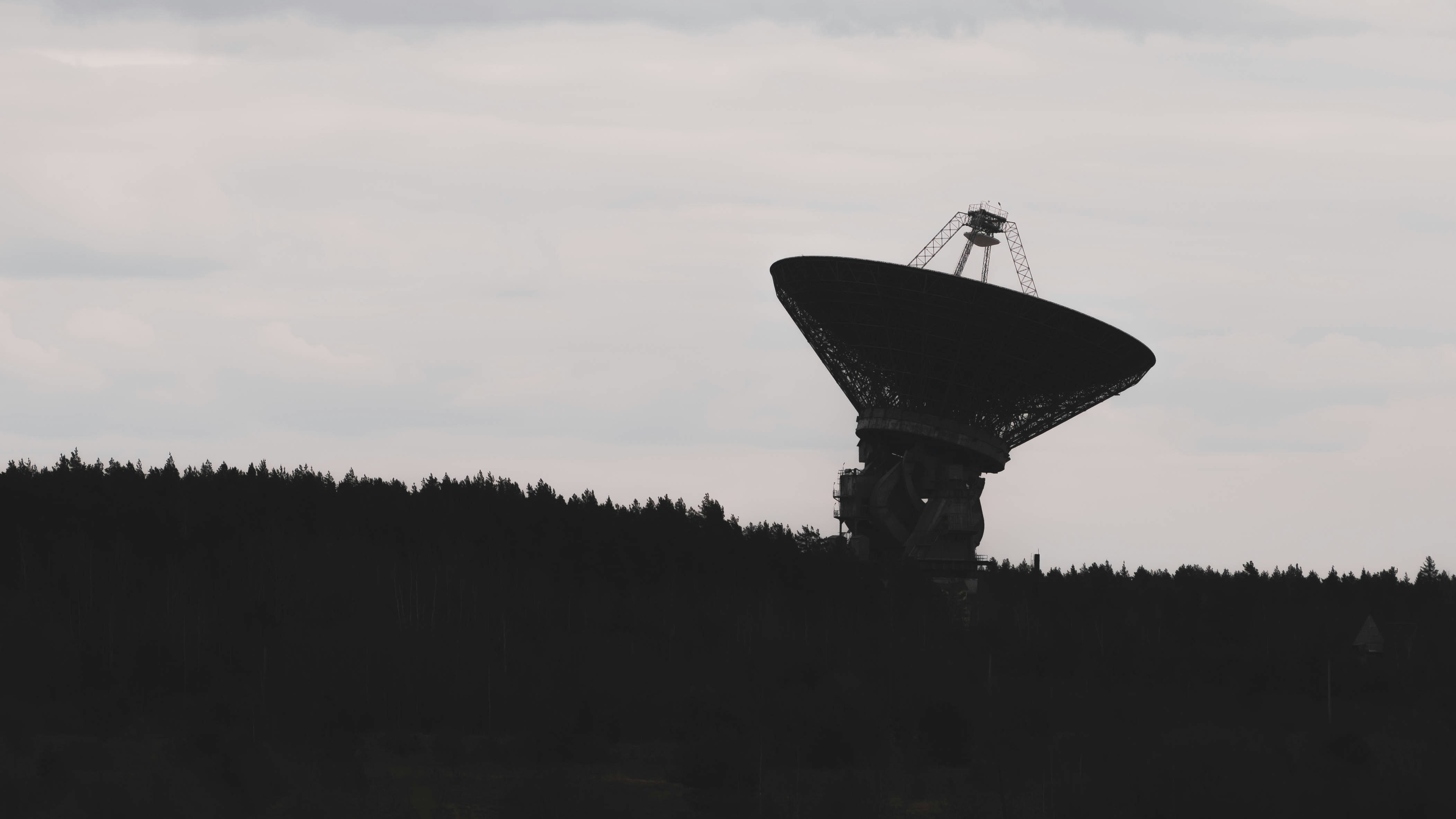 A radio telescope dish silhouetted against a pale grey sky